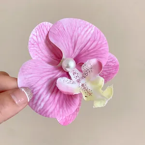 Détail d'une pince à cheveux orchidée rose avec une perle sur un fond beige neutre.
