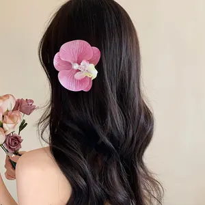 Vue détaillée d'une pince à cheveux orchidée rose avec perle sur longs cheveux ondulés.