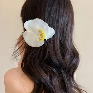 Gros plan d'une pince à cheveux orchidée blanche sur de longs cheveux sombres et ondulés