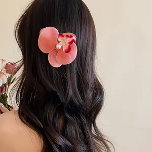 Détail d'une élégante pince à cheveux orchidée rose avec perle sur des cheveux longs.