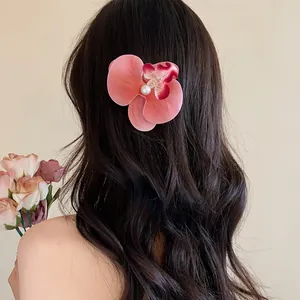 Gros plan d'une pince à cheveux orchidée rose avec perle sur de longs cheveux ondulés.