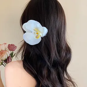 Détail d'une pince à cheveux orchidée blanche sur cheveux longs ondulés, style doux.