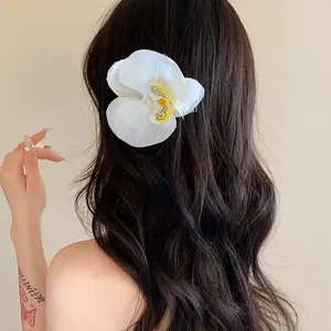 Vue détaillée d'une pince à cheveux orchidée blanche portée sur de longs cheveux ondulés.