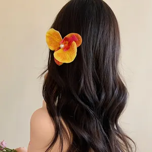 Pince à cheveux fleur d'orchidée avec perle montrée sur de longs cheveux bruns ondulés