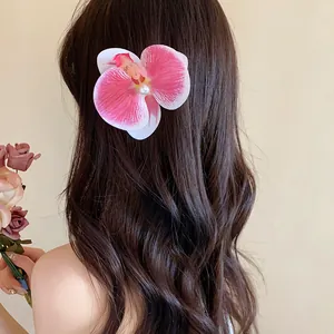 Vue détaillée d'une pince à cheveux en forme d'orchidée rose avec perle sur cheveux ondulés.