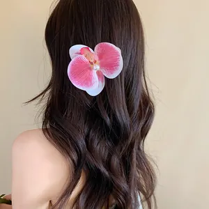 Détail d'une pince à cheveux orchidée rose avec perle sur de longs cheveux ondulés.