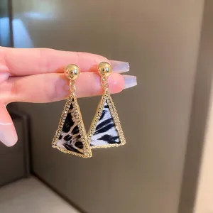 Primo piano di orecchini a triangolo geometrici dorati con stampa leopardata e strass.
