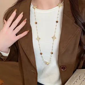 Detail of a vintage-style gold cross sweater chain with tiger eye beads on a model.