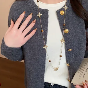 Detailed close-up of a vintage style cross long necklace worn over a grey knitted cardigan
