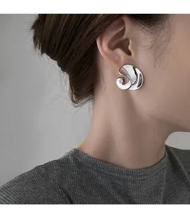 Dettaglio di orecchino a perno a spirale in metallo argento dallo stile minimalista
