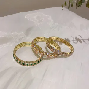 Vista dettagliata di tre lussuosi bracciali dorati con zirconi su panno di seta bianca