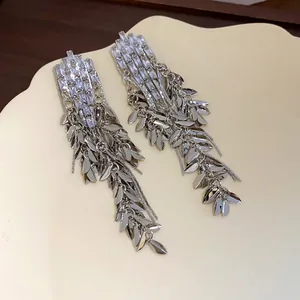 Detail view of silver zircon wheat leaf tassel drop earrings on a ceramic plate