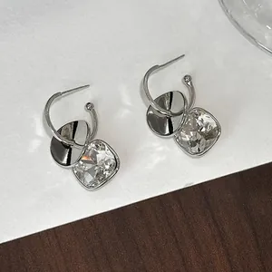 Primo piano degli orecchini a cerchio a C in argento con pendenti in cristallo quadrato.
