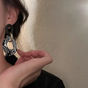 Detalle de elegantes pendientes retro de acrílico con estampado de cebra en una modelo