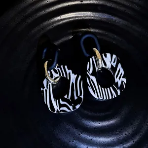 Primer plano de pendientes retro de acrílico con rayas de cebra y detalles dorados