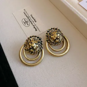 Primo piano di orecchini vintage a testa di leone in oro con doppi cerchi pendenti.