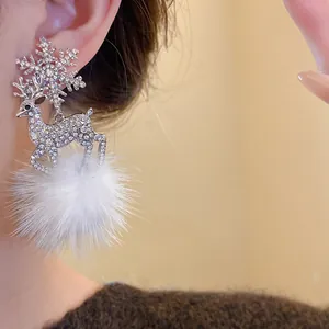 Close-up detail of sparkling reindeer and snowflake earrings with soft white fur ball