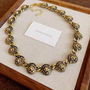 Dettaglio di medaglioni vintage a testa di leone su una collana a maglia grossa dorata.
