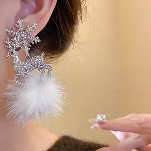 Detailed close-up of sparkling reindeer and snowflake earrings with white fur pom-poms