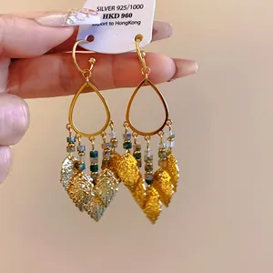 Macro view of bohemian gold teardrop earrings featuring beads and leaf-shaped tassels