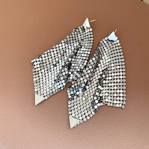Detail shot of silver triangle metallic mesh tassel earrings on textured brown background.
