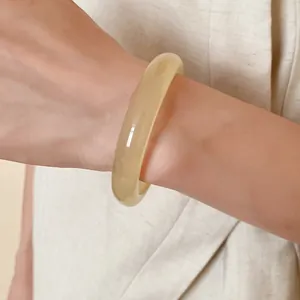 Minimalist cream resin bangle shown on a wrist against an elegant fabric background.