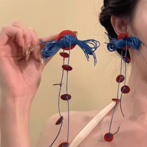 Pendientes de borlas bohemias rojas y azules usados por una modelo en vacaciones