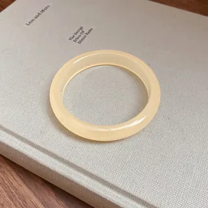Close-up of a minimalist round resin bangle in creamy yellow on a textured book cover