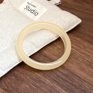 Detailed close-up view of a minimalist cream resin bangle resting on a soft fabric storage pouch