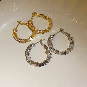 Detail shot of elegant gold and silver zircon hoop earrings on white ceramic dish