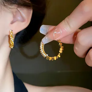 Macro detail of gold hoop earring with sparkling zircon and disc accents on silver needle