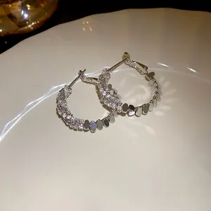 Close-up detail of silver-tone hoop earrings featuring sparkling zircons and polished metal discs