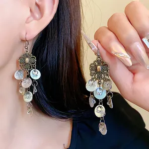 Macro detail of Bohemian vintage flower tassel earrings with shell charms worn by a model
