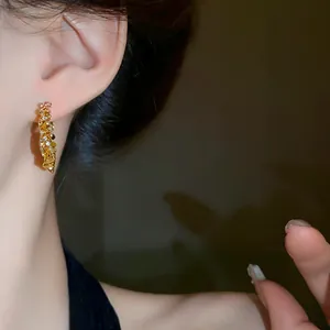 Close-up of elegant gold hoop earrings with sparkling zircon stones on a model's ear