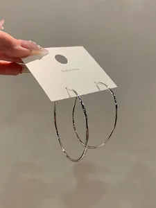 Detailed view of large minimalist polished silver hoop earrings on a white display card