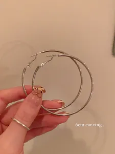 Close-up of 6cm large silver hoop earrings held by hand for size scale