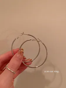 Detailed view of 5cm large silver metallic hoop earrings held by a hand for scale