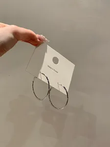 Detailed close-up of large polished silver hoop earrings on a minimalist display card.