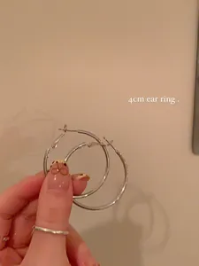 Detailed macro shot of 4cm minimalist silver-tone metal hoop earrings held by hand