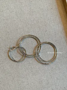 Close-up of minimalist silver metal hoop earrings in three sizes on beige fabric