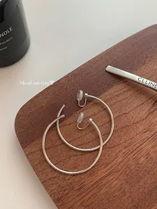 Close-up of large silver metal hoop earrings with comfortable clear ear clips on wood