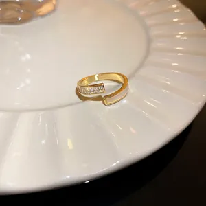 Primer plano de un anillo geométrico dorado con circonitas e incrustación de nácar blanco