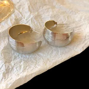 Primo piano di orecchini a lobo a forma di C color argento con dettagli a righe fini.