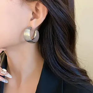 Primo piano di un orecchino a cerchio a forma di C argento con elegante trama spazzolata