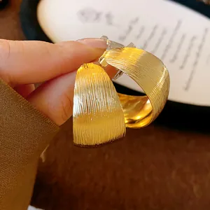 Dettaglio di orecchini a cerchio a C dorati con strisce geometriche e perni in acciaio