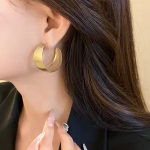 Primo piano di eleganti orecchini a cerchio a C dorati con texture rigata su modella