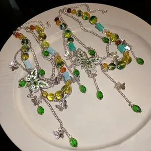 Collana con farfalla smaltata e perline di vetro verdi su un piatto bianco pulito