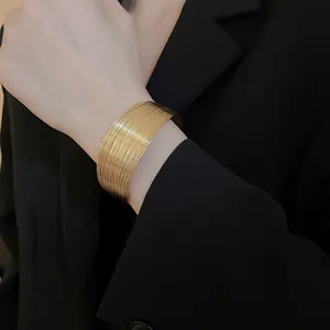 Detailed view of a wide gold-toned multi-layer textured metal cuff bracelet on wrist