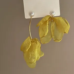 Detail of asymmetric yellow chiffon flower earrings with elegant white pearl studs.