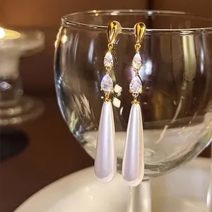 Détail de boucles d'oreilles dorées avec zircone en goutte et perle nacrée.
